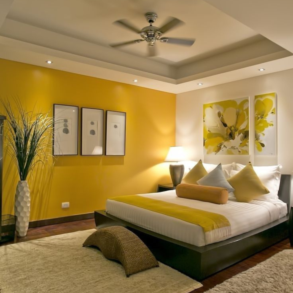 Yellow and white color wall paintings of a bedroom with a ceiling fan and wall paintings and also have a interior plant in a corner.